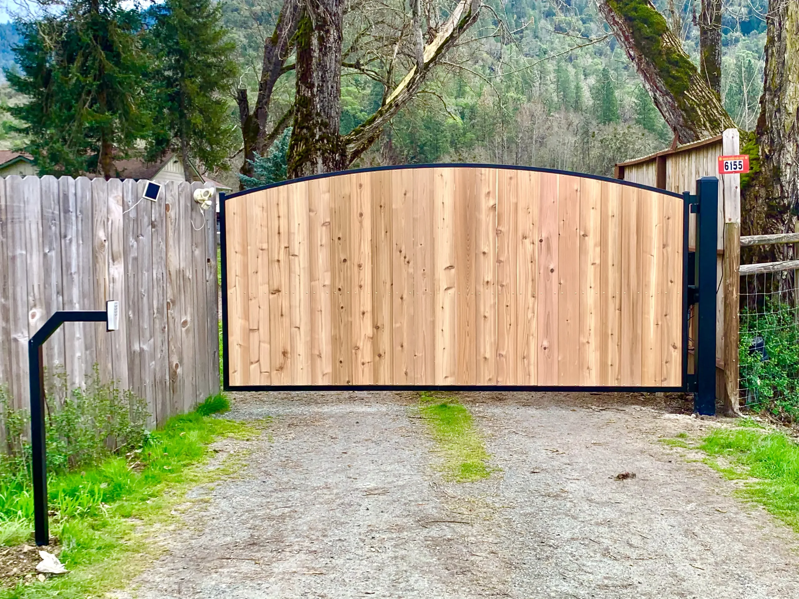 , installed next to a wooden fence on a gravel driveway.