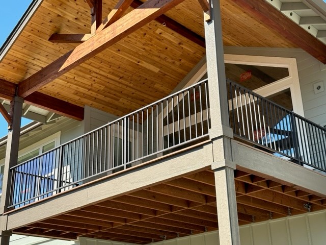 The image shows an elevated wooden deck featuring a dark metal picket railing and a timber-paneled roof overhang